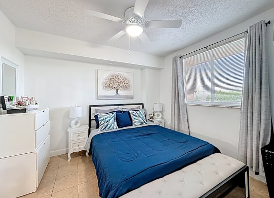 A bedroom with a blue bedspread and white furniture.