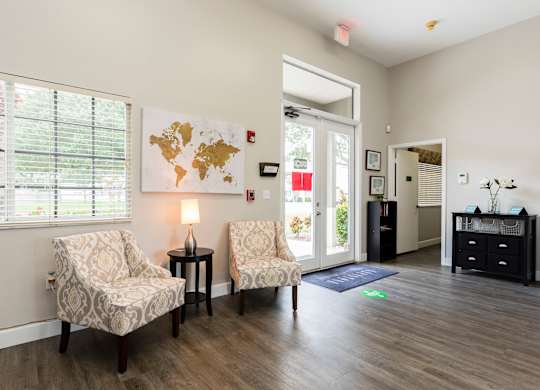 A living room with two chairs, a table with a lamp, and a world map on the wall.