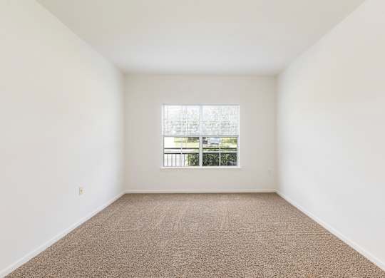A room with a carpeted floor and a window overlooking a balcony.