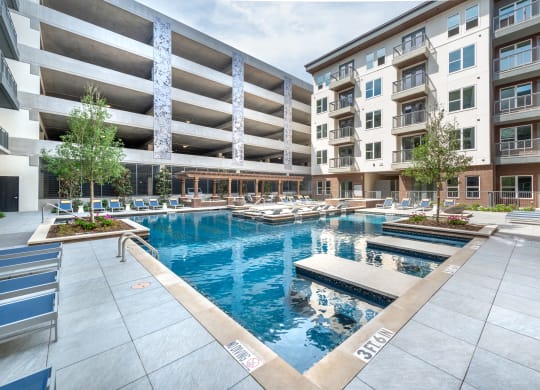 Pool courtyard with pool in the middle and chairs around pool with view of apartment building and balconies and parking garage behind pool