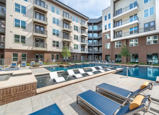 Pool courtyard with pool in the middle and chairs around pool with view of apartment building and balconies and tanning chairs