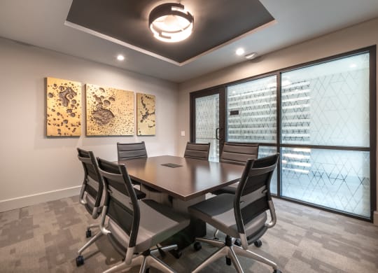 Conference room with wooden table and black leather chairs and gold artwork on wall with glass windows and door that have patterns on them for privacy