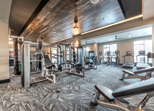 Gym area with view of a variety of weight machines and wooden panel ceilings and gray patterned carpet