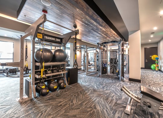 Gym area with view of a variety of weight machines and training equipment with wooden panel ceilings and gray patterned carpet