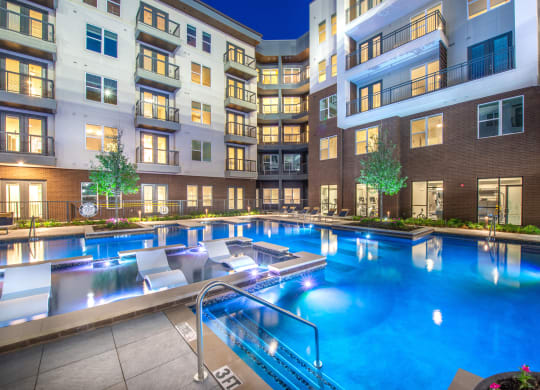 Courtyard pool area during nighttime with bright lights in water and view of surrounding apartments and balconies