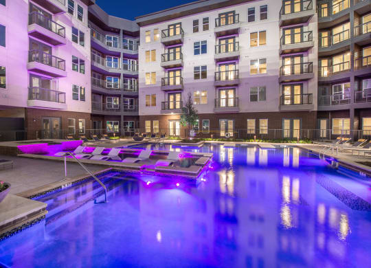 Courtyard pool area during nighttime with purple lights in water and view of surrounding apartments and balconies