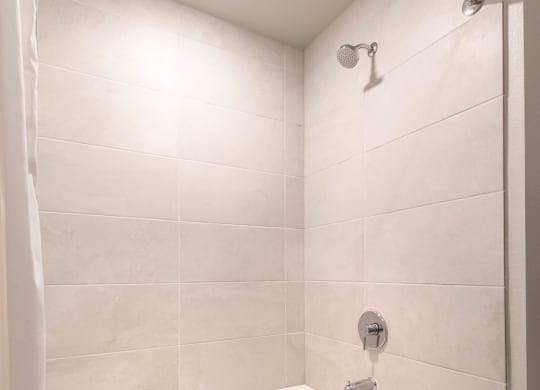 Large white bathtub with gray tile and silver showerhead