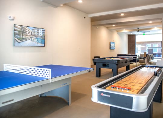Outdoor covered patio with view of shuffle board table and ping pong table to the left with a pool table behind and a TV mounted on the left wall