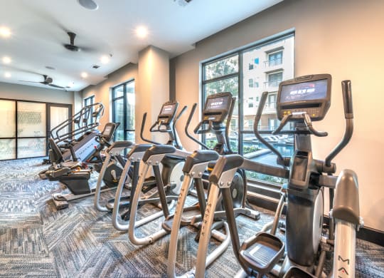 Community gym of with wall lined of ellipticals and other cardio machines looking out into a window that faces the pool