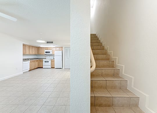 A kitchen with white appliances and a staircase.