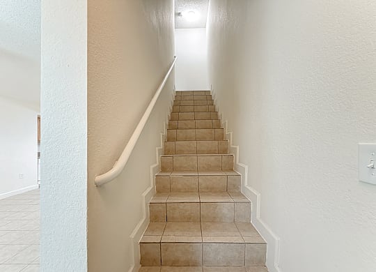 A staircase with beige tiles and white railings.