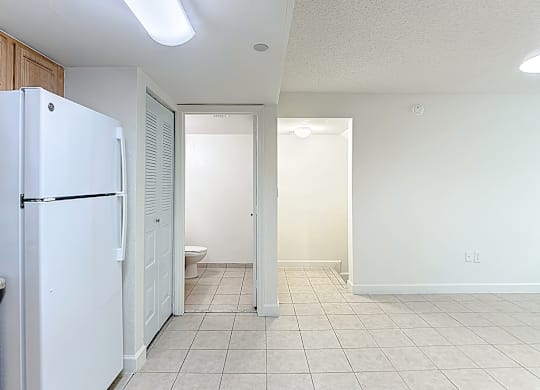 A white refrigerator is in a kitchen with white walls and tile flooring.