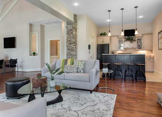 Clubhouse Seating Area with Grey Couches Triangle Glass Coffee Table with Clubhouse Kitchen with Black Breakfast Bar Black Appliances and White Cabinets in the Background