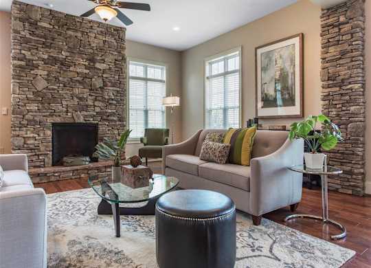 Clubhouse Seating Area with Grey Couches Triangle Glass Coffee Table Brick Fireplace with Windows and Decorations