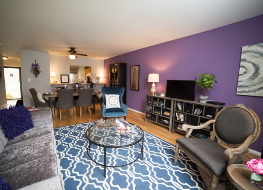 Living room with sofa and arm chairs with blue rug and a ceiling fan in the background with above the dinning table.
