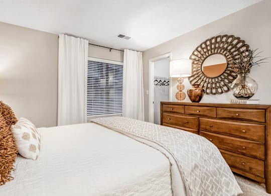 A bedroom with a large bed, a wooden dresser, and a mirror on the wall at Paces Pointe Apartment Homes, North Carolina