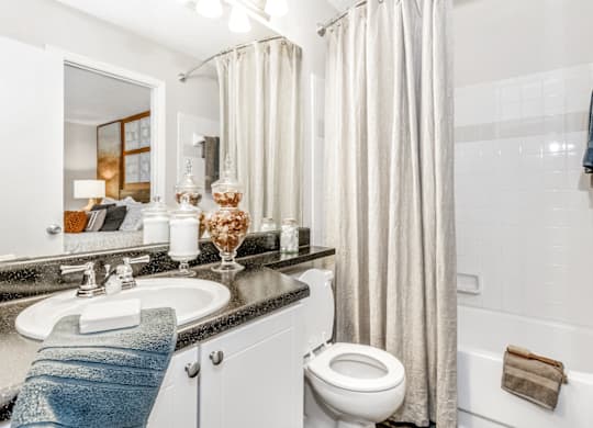 A bathroom with a white toilet, a sink, a bathtub, and a shower curtain at Paces Pointe Apartment Homes, North Carolina