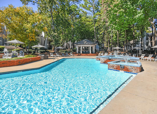 A large swimming pool surrounded by trees and a gazebo at Paces Pointe Apartment Homes, Matthews, NC