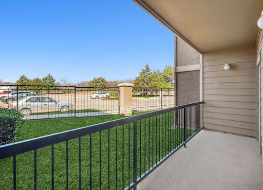 A balcony with a black railing overlooking a parking lot.