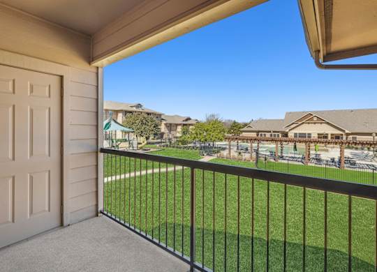 A balcony with a white door and a black railing overlooking a green lawn and houses.