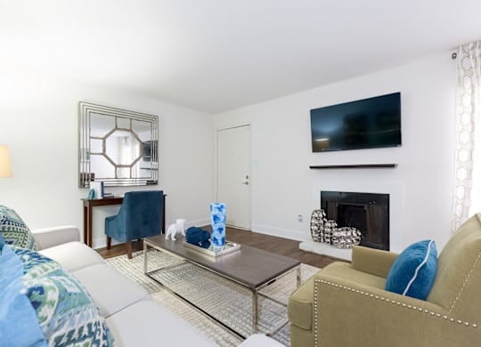 A living room with a white couch, a tan armchair, a glass coffee table, and a fireplace at Regency Park Apartment Homes, Raleigh, North Carolina