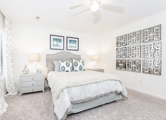 A bedroom with a large bed, a ceiling fan, and a wall of framed pictures at Regency Park Apartment Homes, North Carolina