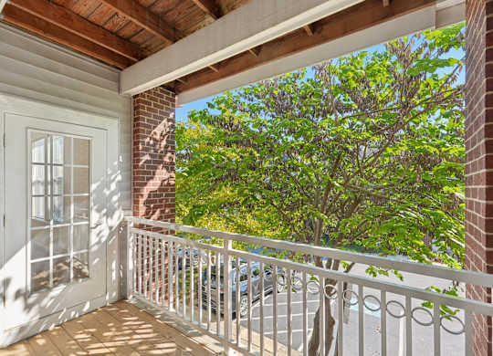 A balcony with a white railing and a view of a tree and a building.