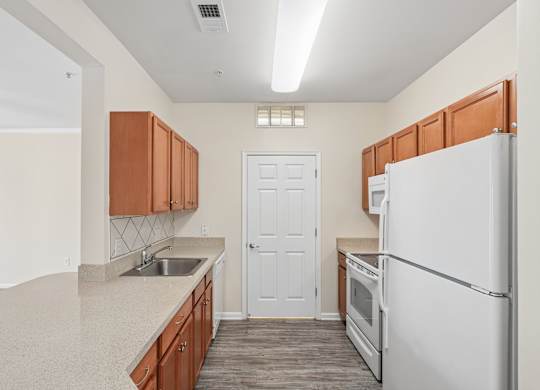 A kitchen with a white refrigerator, wooden cabinets, and a white door.