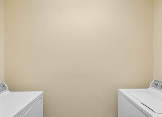 Two white washing machines in a room with beige walls.