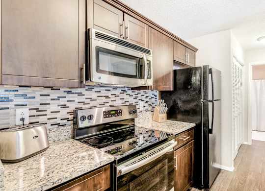 A kitchen with a black refrigerator, stove, and microwave.