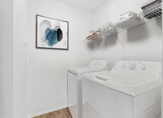 A white washing machine in a small laundry room with a picture on the wall.