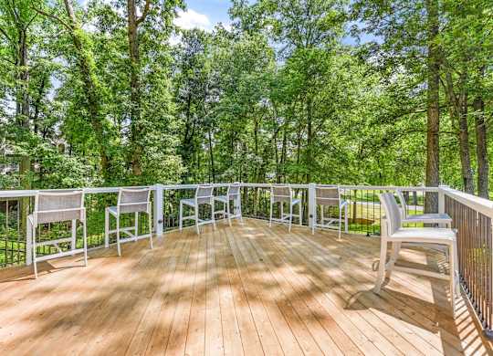 A wooden deck with white chairs and a railing overlooking a forest.