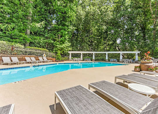 A pool surrounded by trees and lounge chairs.