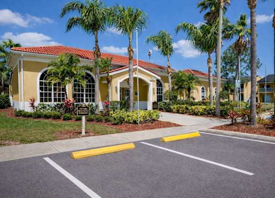 A yellow building with a red roof and palm trees in front.