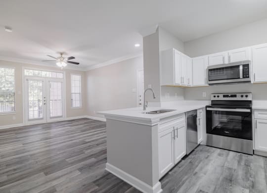 kitchen with stainless appliances, white cabinetry, and hardwood style flooring with living room in the background