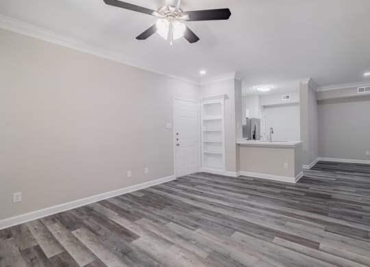 an empty living room with a ceiling fan and built-in shelving