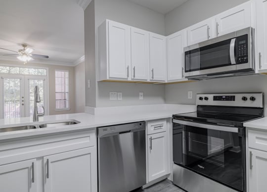 kitchen with stainless appliances, white cabinetry, and hardwood style flooring with living room in the background