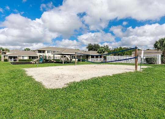 A playground with a blue fence and a sandbox in the middle of a grassy area.