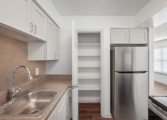 A kitchen with a stainless steel refrigerator and a sink with a brick backsplash.