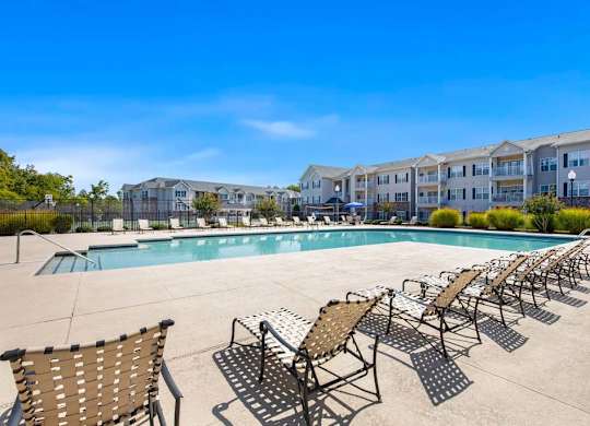 A pool surrounded by sun loungers and chairs with apartment buildings in the background at Ethan Pointe Apartments, North Carolina, 27215