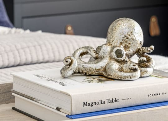 a pile of books on a bed with an octopus statue on top of them