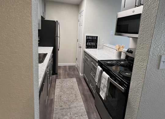 A kitchen with a black refrigerator, stove, and a rug on the floor.