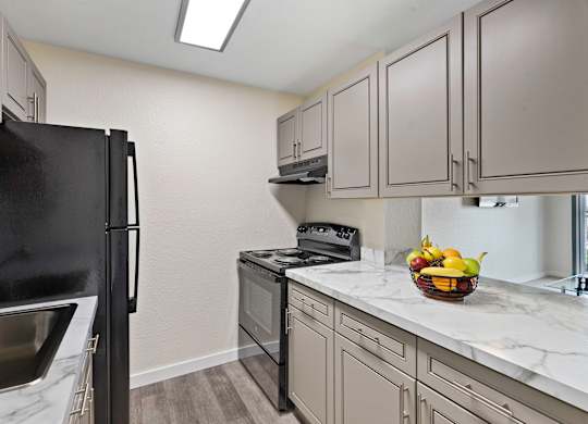 Kitchen with Grey Cabintery, Plank Flooring, and Efficient Appliances, Providing View into Spacious Living Area at Campo Basso Apartment Homes, Lynnwood, 98087