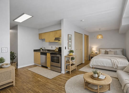 A modern kitchen with wooden cabinets and a white countertop is adjacent to a cozy bedroom with a large bed and a nightstand.