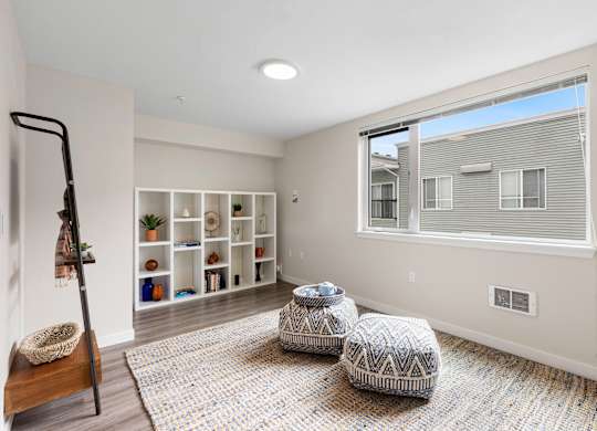 Cozy Living Area with Plank Flooring, Spacious Cozy Rugs, White Bookshelving, a large window and two stools in the middle of the room at Arabella Apartment Homes, Washington, 98155