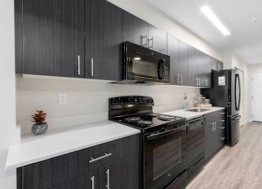 a kitchen with dark cabinets, white countertops, efficient appliances, and plank flooring at Arabella Apartment Homes, Washington, 98155