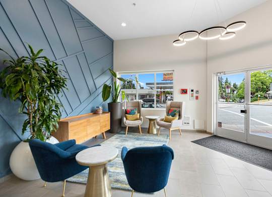 Lobby Area with blue chairs, textured dark blue accent wall, and a wooden desk with a plant in the corner at Arabella Apartment Homes, Shoreline