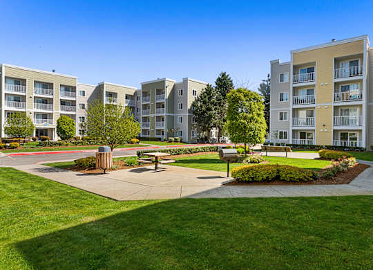 an open area with benches and trees in front of an apartment building  at Camelot Apartment Homes, Everett