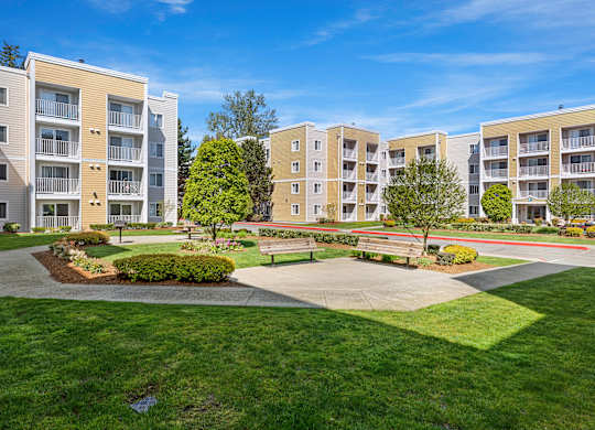 an exterior view of an apartment complex with green grass and trees  at Camelot Apartment Homes, Everett, WA, 98204