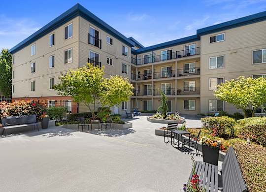 a courtyard with a paved lounge area and benches with landscaped trees and bushes at Guinevere Apartment Homes, Seattle, WA